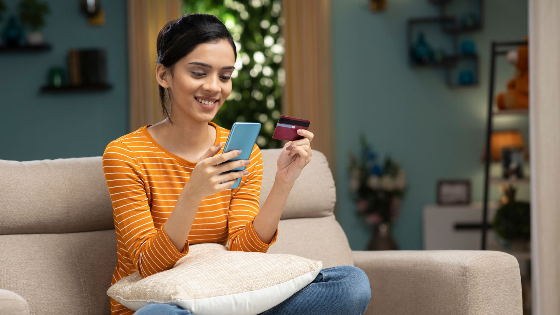 Woman sitting down on couch with phone and credit card in hand.